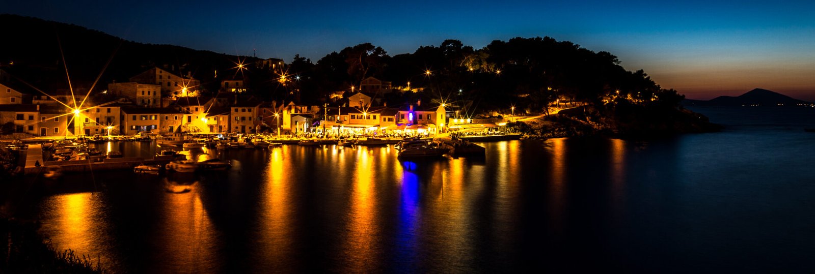 illuminated-buildings-by-sea-against-sky-night