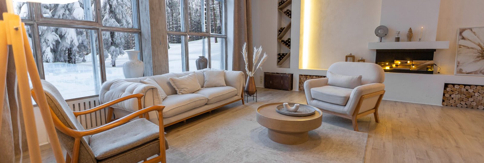 cozy warm home interior of a chic country chalet with a huge panoramic window overlooking the winter forest. open plan, wood decoration, warm colors and a family hearth